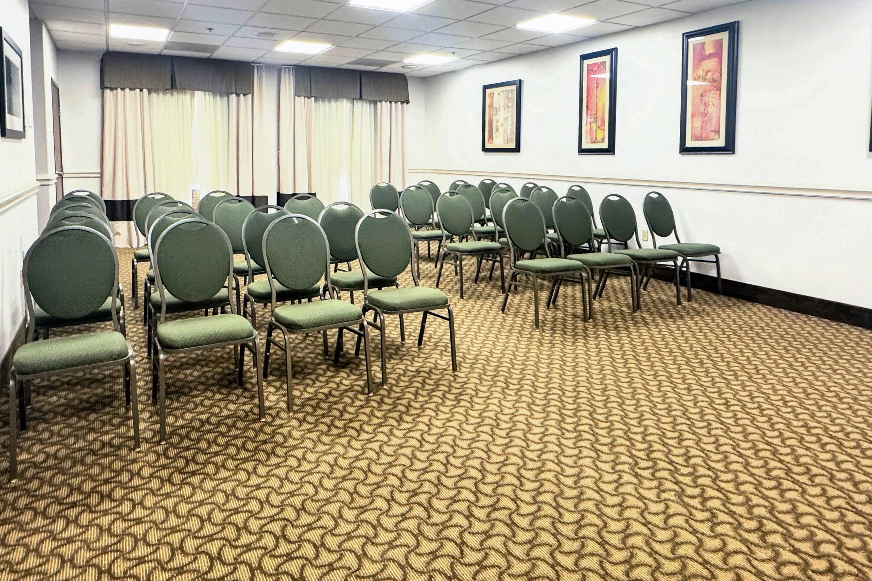 Une salle de conférence avec des rangées de chaises vertes et un tapis à motifs.