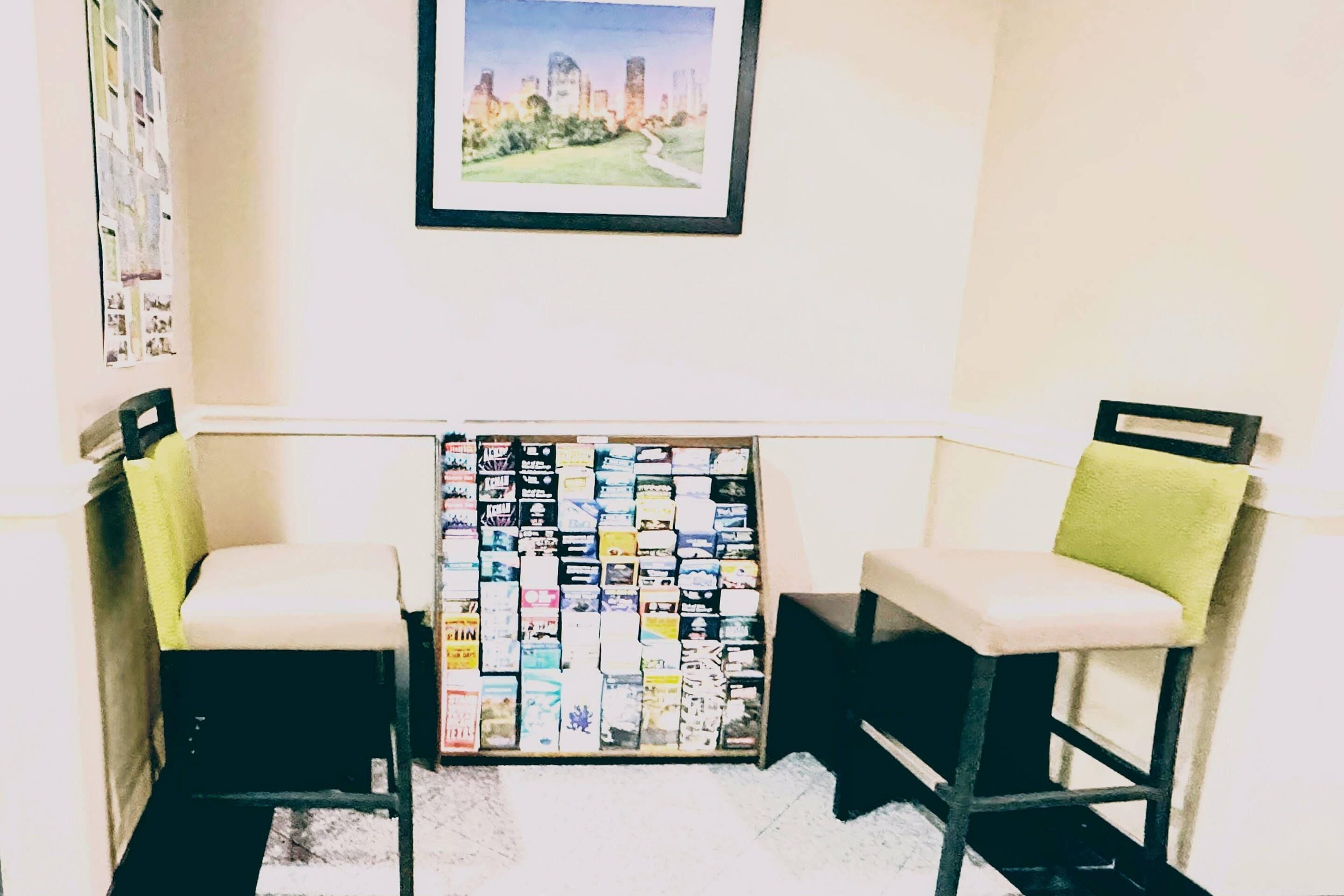 A room with two black chairs with white cushions, a wall-mounted picture of a cityscape, and a bulletin board with various papers and notes.