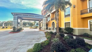 A hotel entrance with a covered walkway, palm trees, and a well-maintained garden. - Comfort Suites Westchase Houston Energy Corridor (Houston)