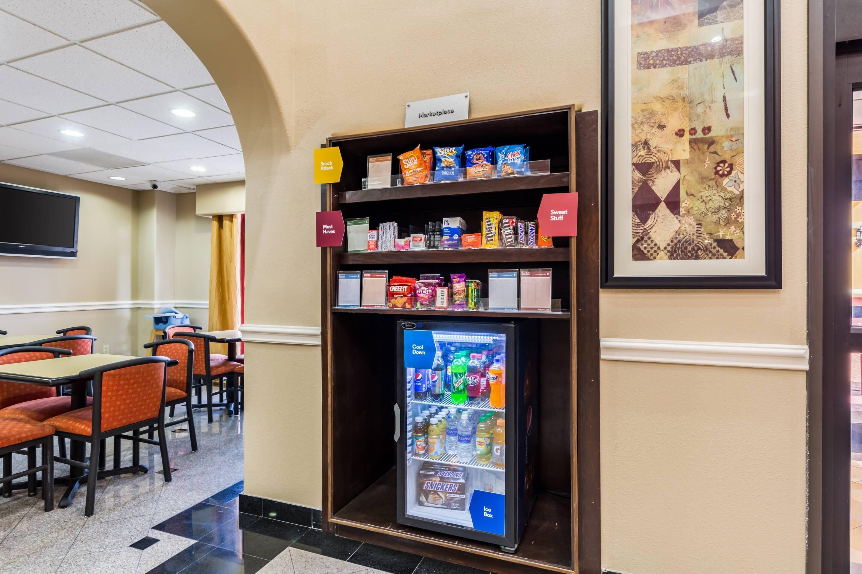Eine Hotellobby mit einer Snackbar, einem mit Getränken und Snacks gefüllten Kühlschrank und einem an der Wand befestigten Fernseher.