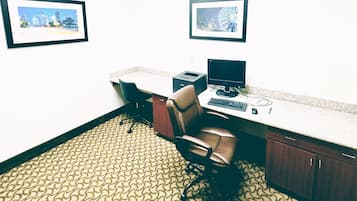 Oficina de hotel con dos cuadros en la pared, un escritorio con computadora, una silla y una alfombra estampada.