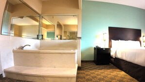 A hotel room with a large mirror, a bathtub, a bed with a dark headboard, and a nightstand with a lamp. - Comfort Suites Westchase Houston Energy Corridor (Houston)