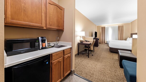 A hotel room with a kitchenette, a bed, a desk, and a bathroom. - Roanoke Suites (Roanoke)