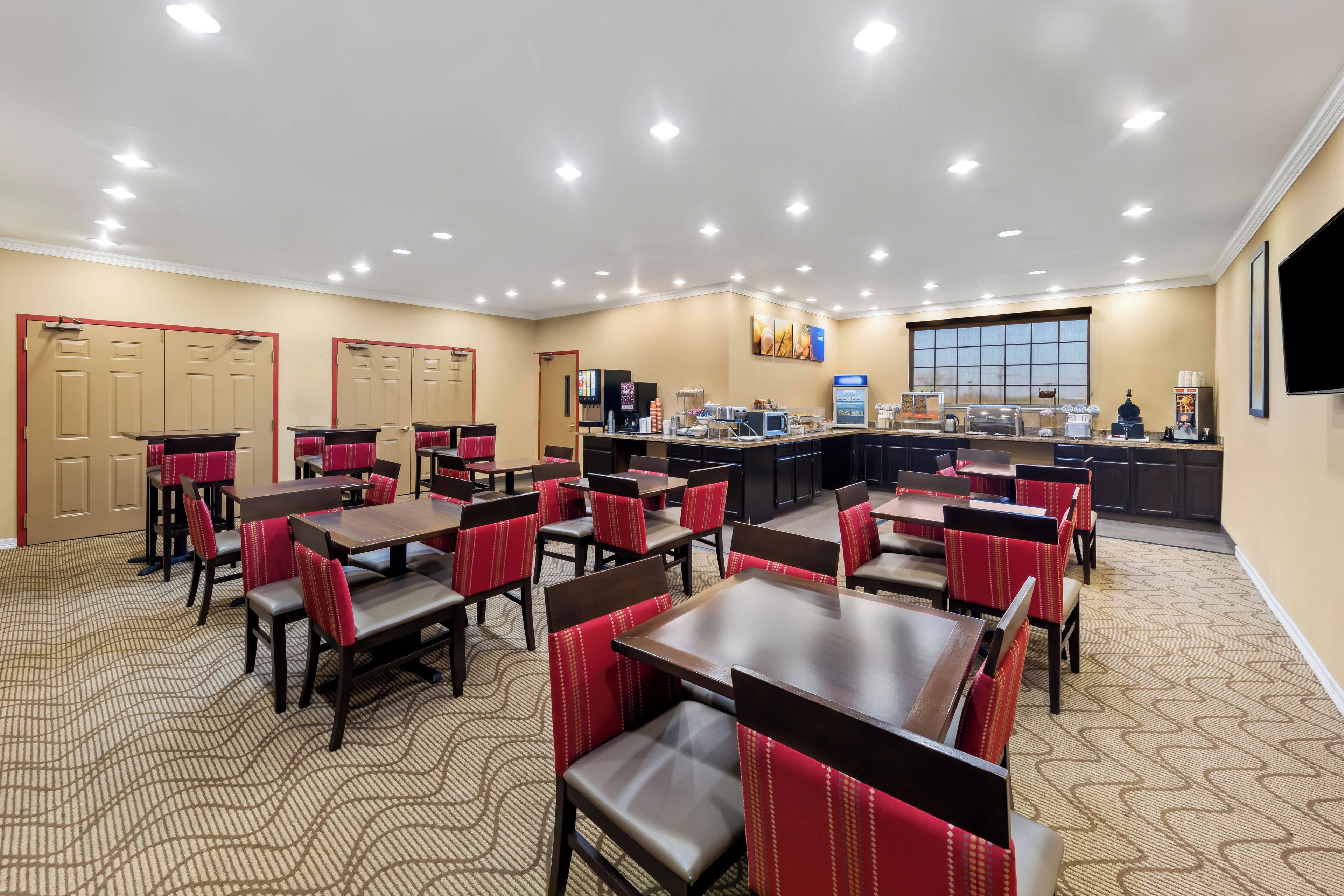 A hotel dining area with multiple tables and chairs, a buffet station, and a large window.