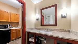 A modern bathroom with a granite countertop sink, a large mirror, and wooden cabinets. - Roanoke Suites (Roanoke)