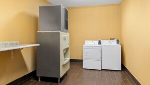 A laundry room with a refrigerator, a water dispenser, and a stacked washer and dryer. - Roanoke Suites (Roanoke)