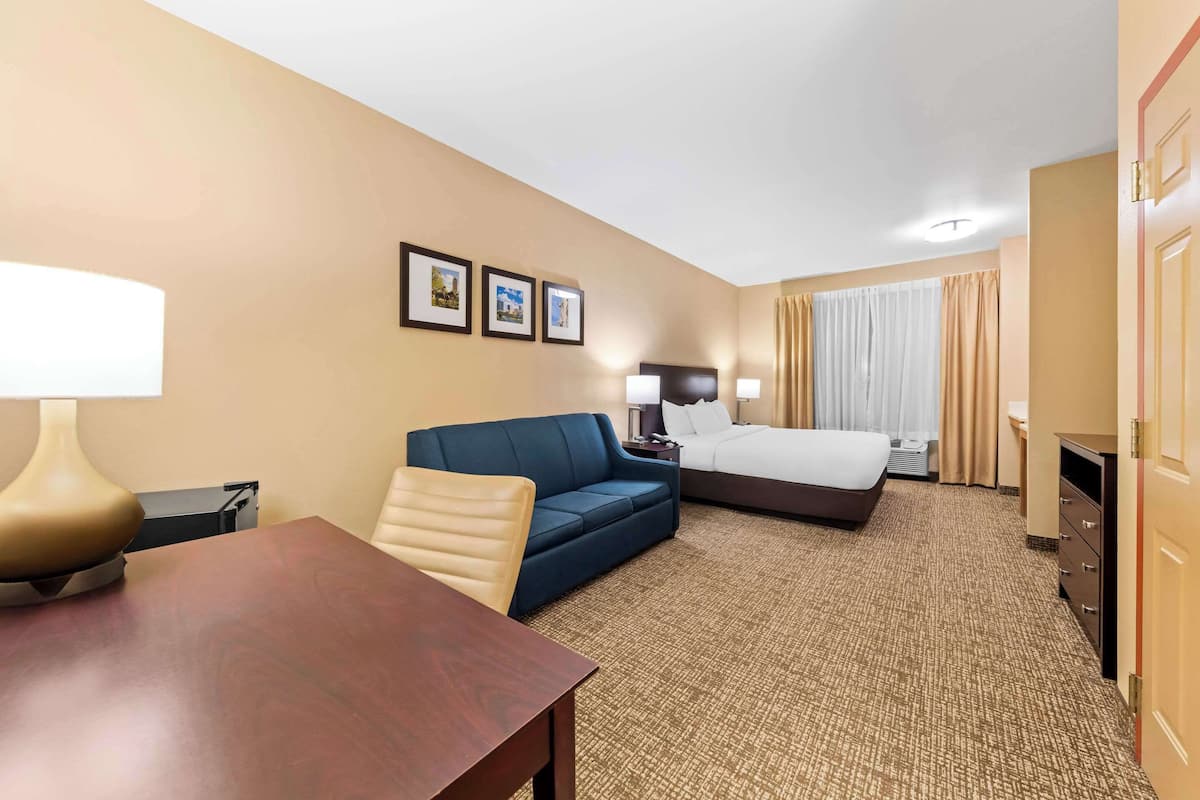Een hotelkamer met een bed, een blauwe bank, een houten tafel en een bureau. Er hangen drie ingelijste foto's aan de muur.