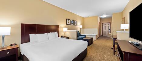 A hotel room with a large bed, bedside tables, a desk with a chair, a television, and a door leading to a bathroom.