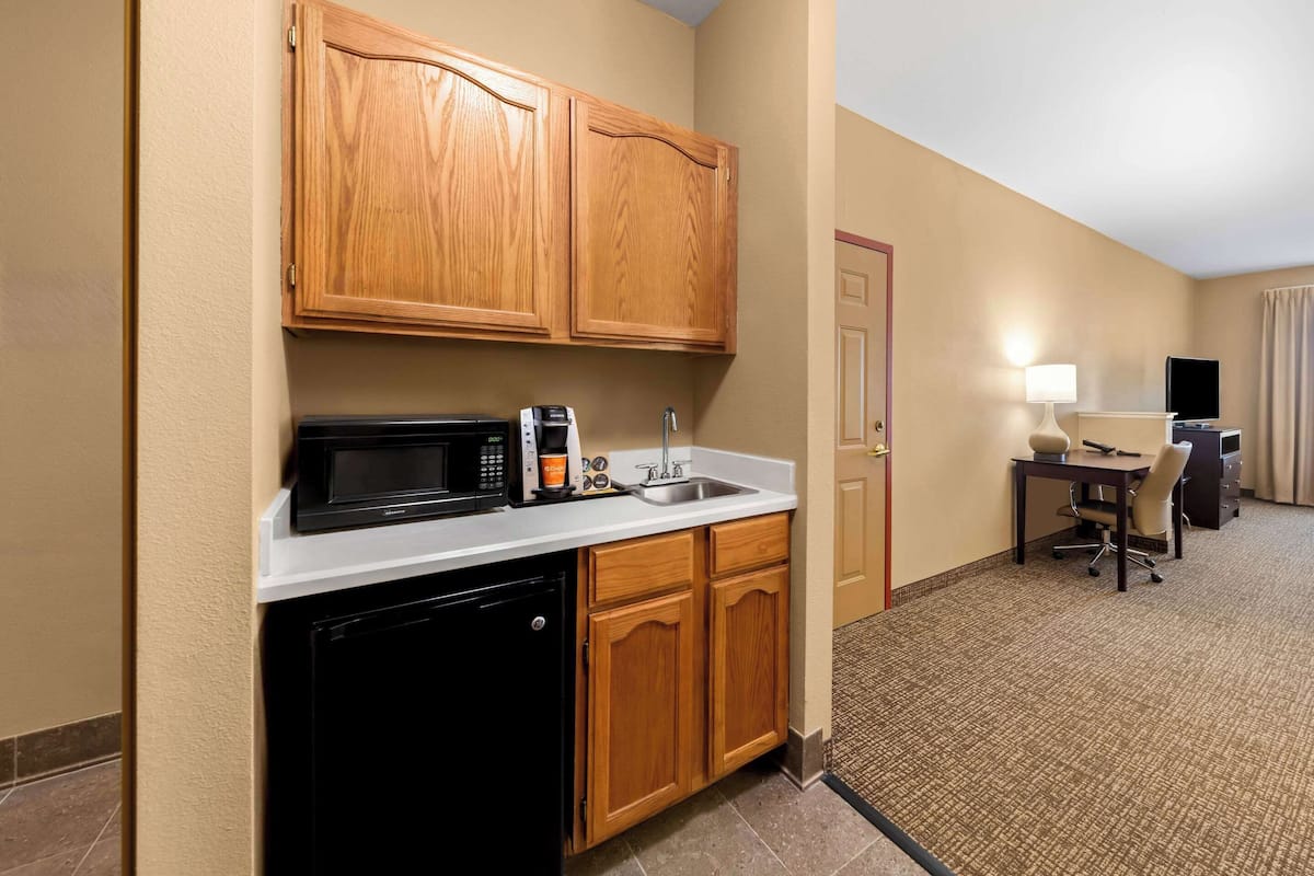 Een compacte hotelkamer met kitchenette, inclusief magnetron, koffiezetapparaat en spoelbak. Er is een bureau met een stoel en een televisie.