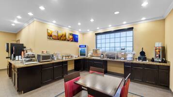 A hotel breakfast area with a long counter, microwave, coffee machine, and seating area.