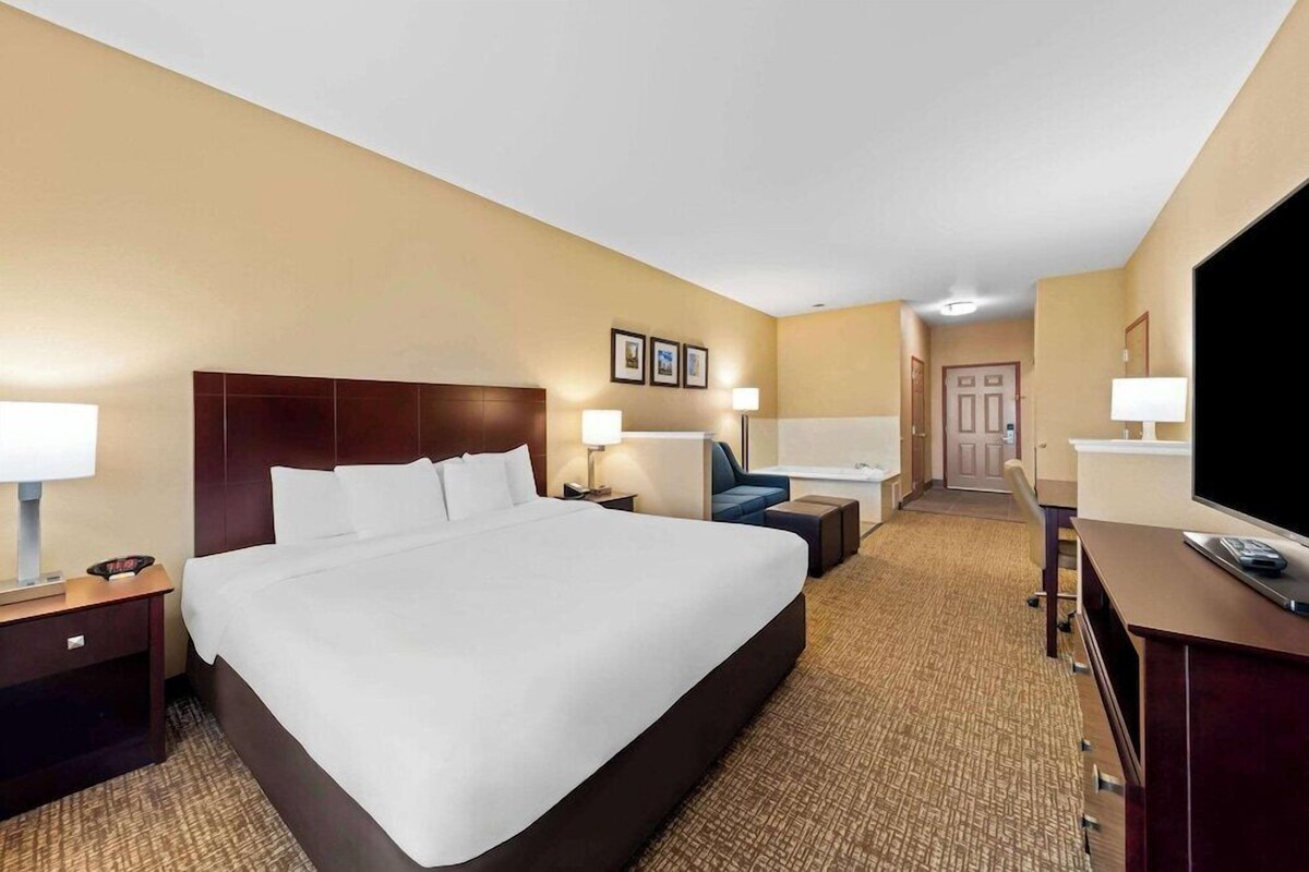 Une chambre d’hôtel avec un grand lit, des tables de chevet, un bureau, une chaise, une télévision et une porte donnant sur une salle de bain.
