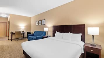 A hotel room with a large bed, a desk with a chair, a blue armchair, and two bedside lamps.