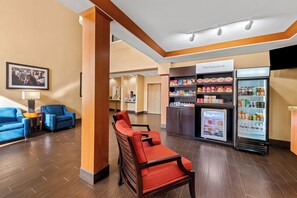 Un hall d’hôtel aménagé avec des sièges, une kitchenette et un réfrigérateur rempli de collations et de boissons.