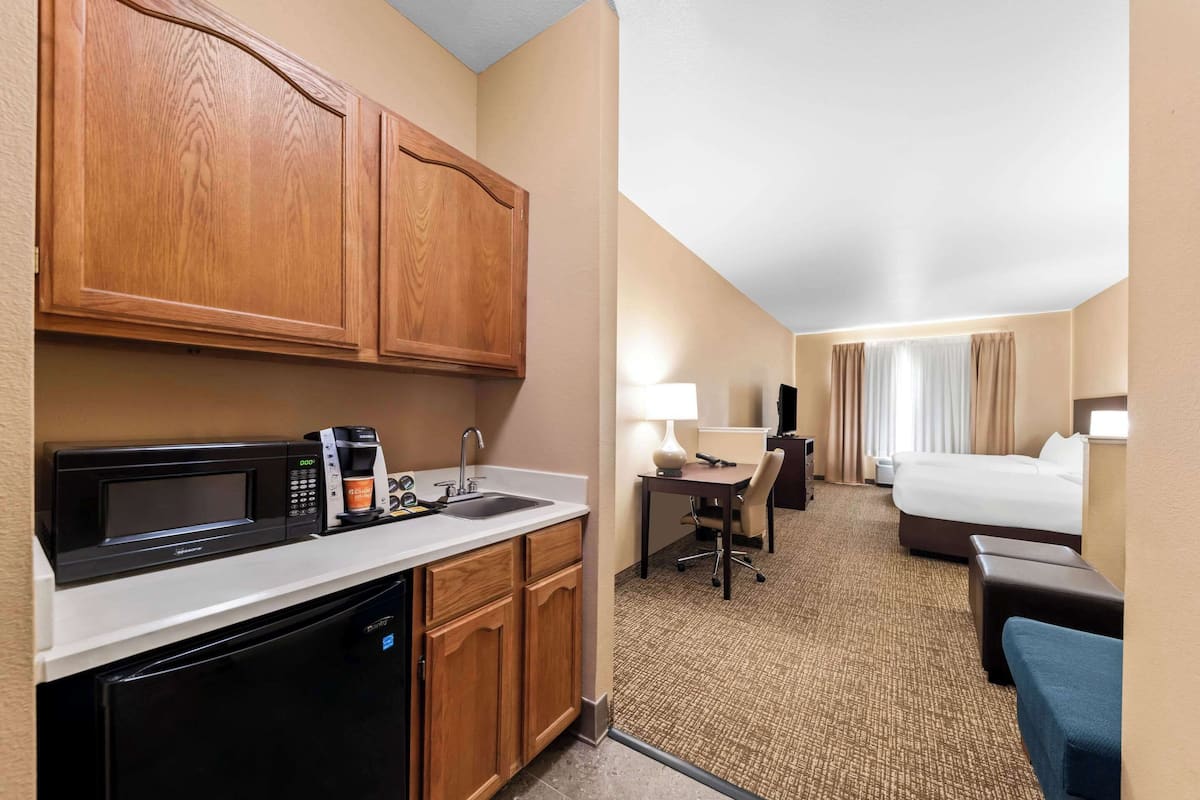Een hotelkamer met een kitchenette, een bed, een bureau en een stoel.
