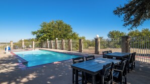 A swimming pool with a surrounding fence, outdoor seating area with tables and chairs, and trees in the background. - Roanoke Suites (Roanoke)