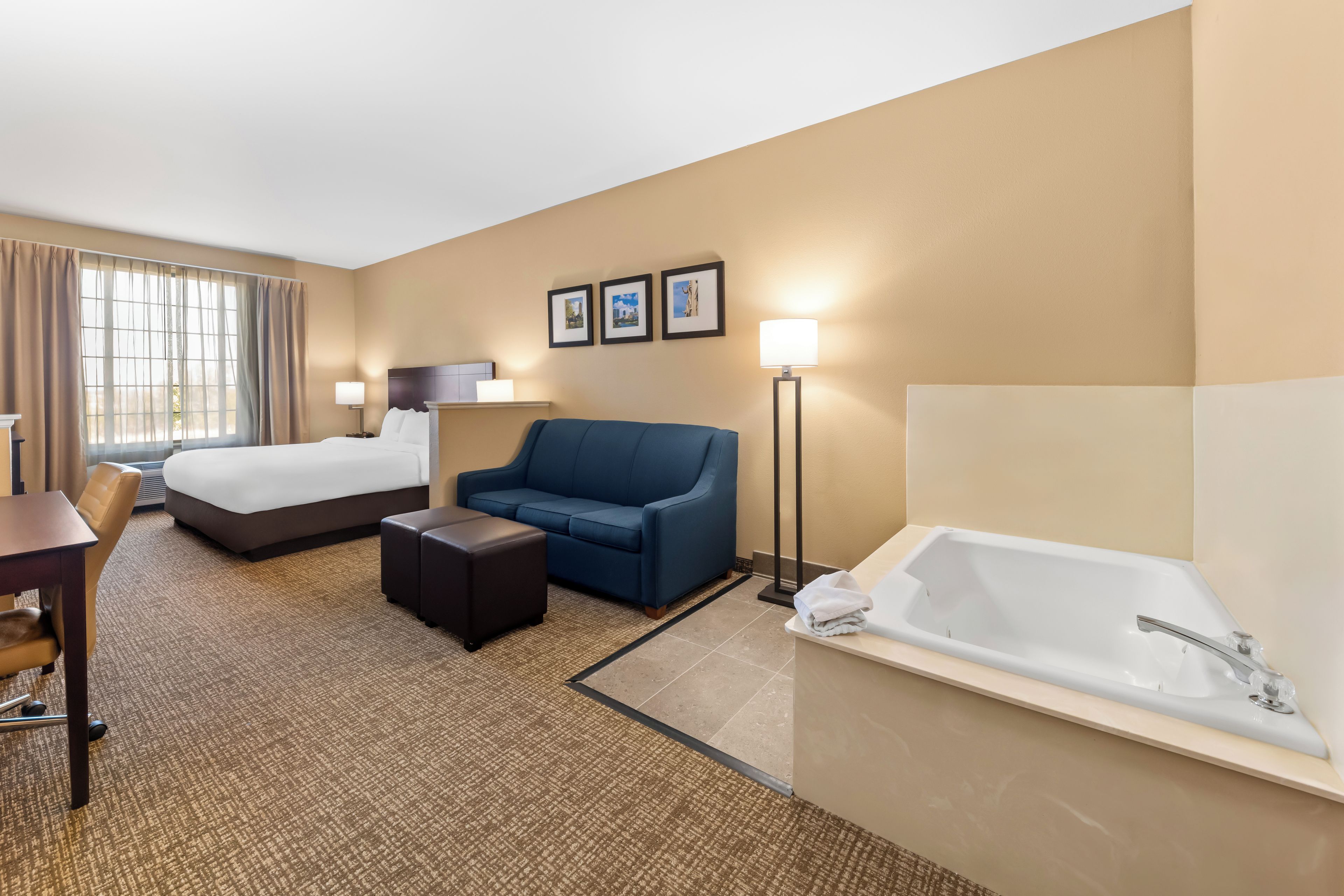 Habitación de hotel con cama, sofá, escritorio, silla, una mesita, lámpara de pie y bañera.