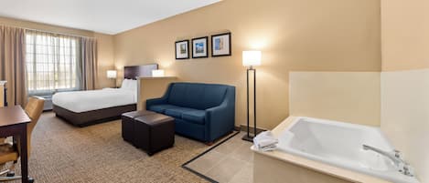 Habitación de hotel con cama, sofá, escritorio, silla, una mesita, lámpara de pie y bañera.