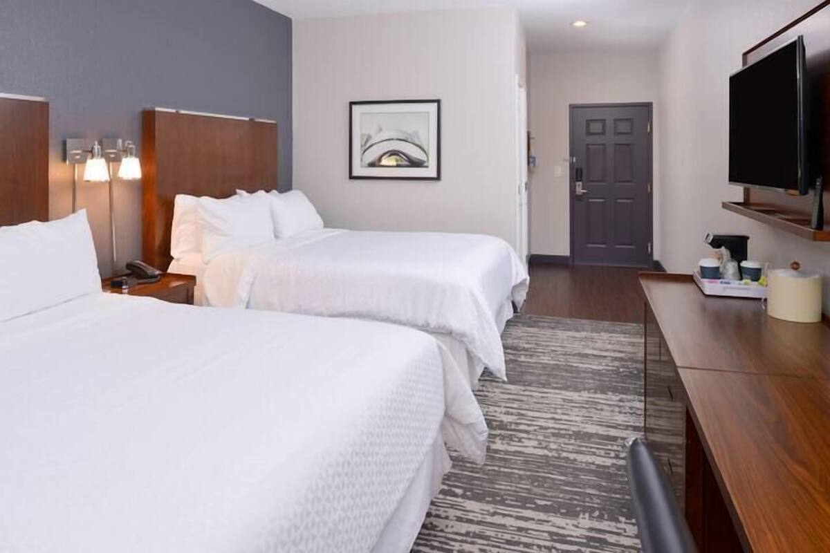 Quarto de hotel com duas camas, uma escrivaninha, televisão e um quadro emoldurado na parede.