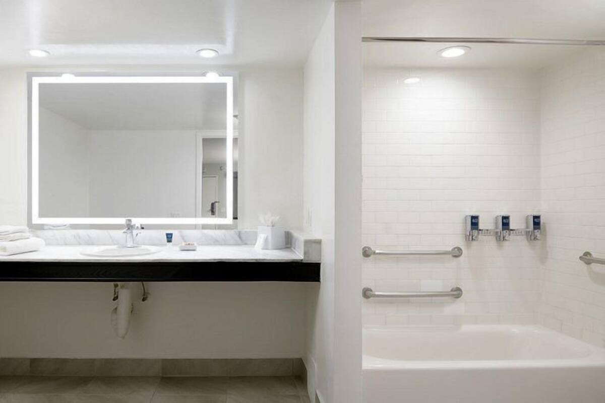 Uma casa de banho moderna com um espelho grande, uma banheira e uma sanita.