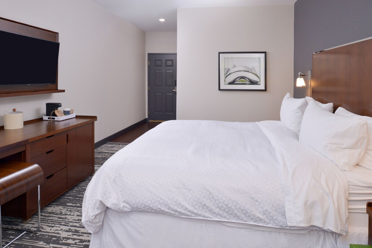 Una habitación de hotel con una cama, un escritorio, un televisor y una puerta.