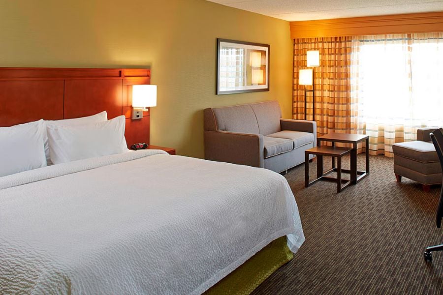 A hotel room with a large bed, a sofa, a small table, and a chair.