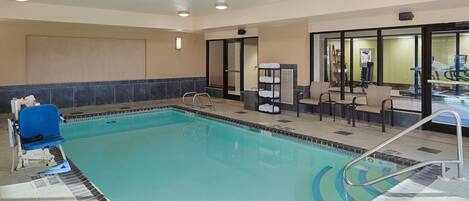 An indoor swimming pool with a blue chair, a changing room, and a seating area with chairs and a table.