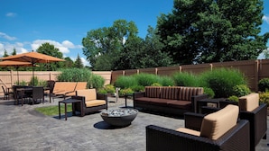 An outdoor patio area with wicker furniture, a fire pit, and a wooden fence. - Courtyard by Marriott Ithaca Airport/University (Ithaca)