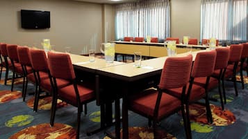 Une salle de conférence avec une longue table, des chaises rouges et un téléviseur fixé au mur.