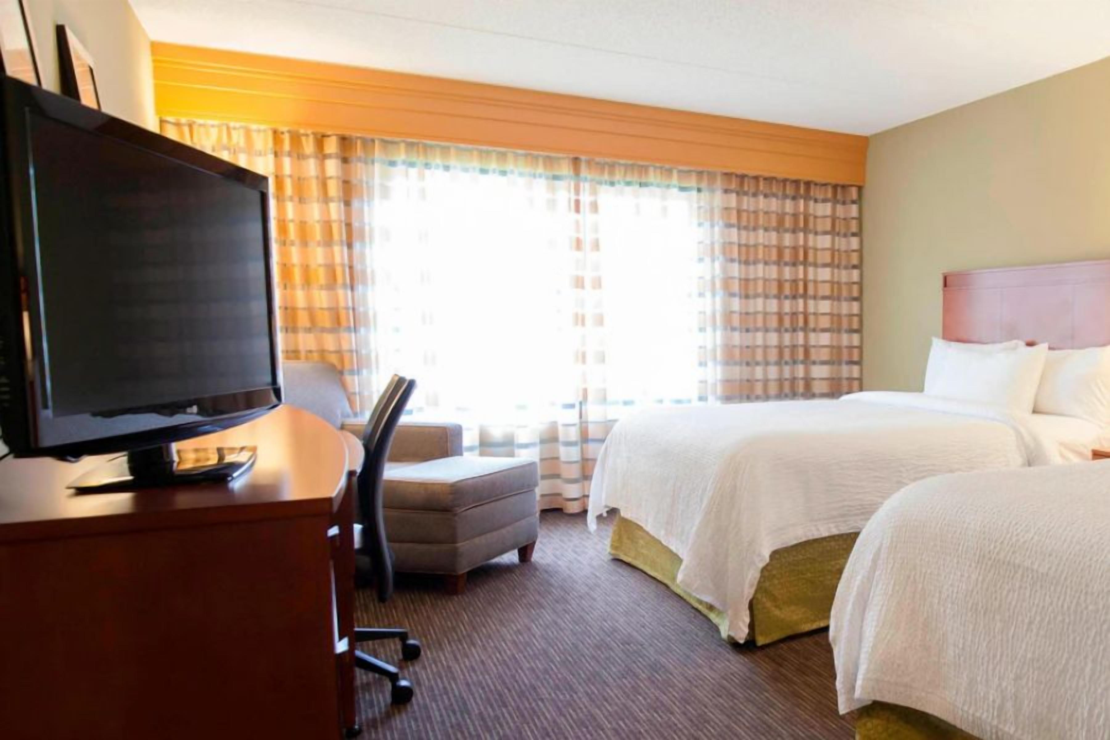 A hotel room with a bed, a desk with a television, a chair, and a window with curtains.