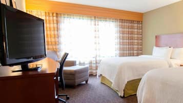 A hotel room with a bed, a desk with a television, a chair, and a window with curtains.
