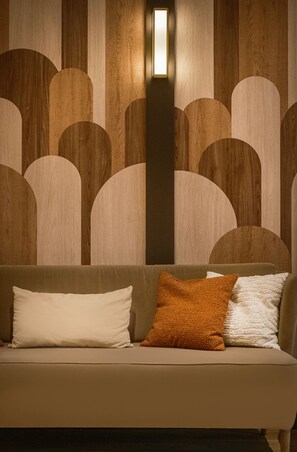 A room with a sofa, two pillows, and a wall with a geometric pattern. - Hôtel Le Monna Lisa by Inwood Hotels (Paris)
