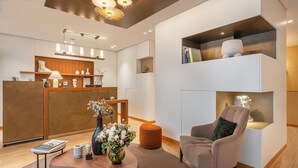 A modern reception area with a wooden reception desk, a seating area with a cushioned chair, and a decorative vase with flowers. - Hôtel Le Monna Lisa by Inwood Hotels (Paris)