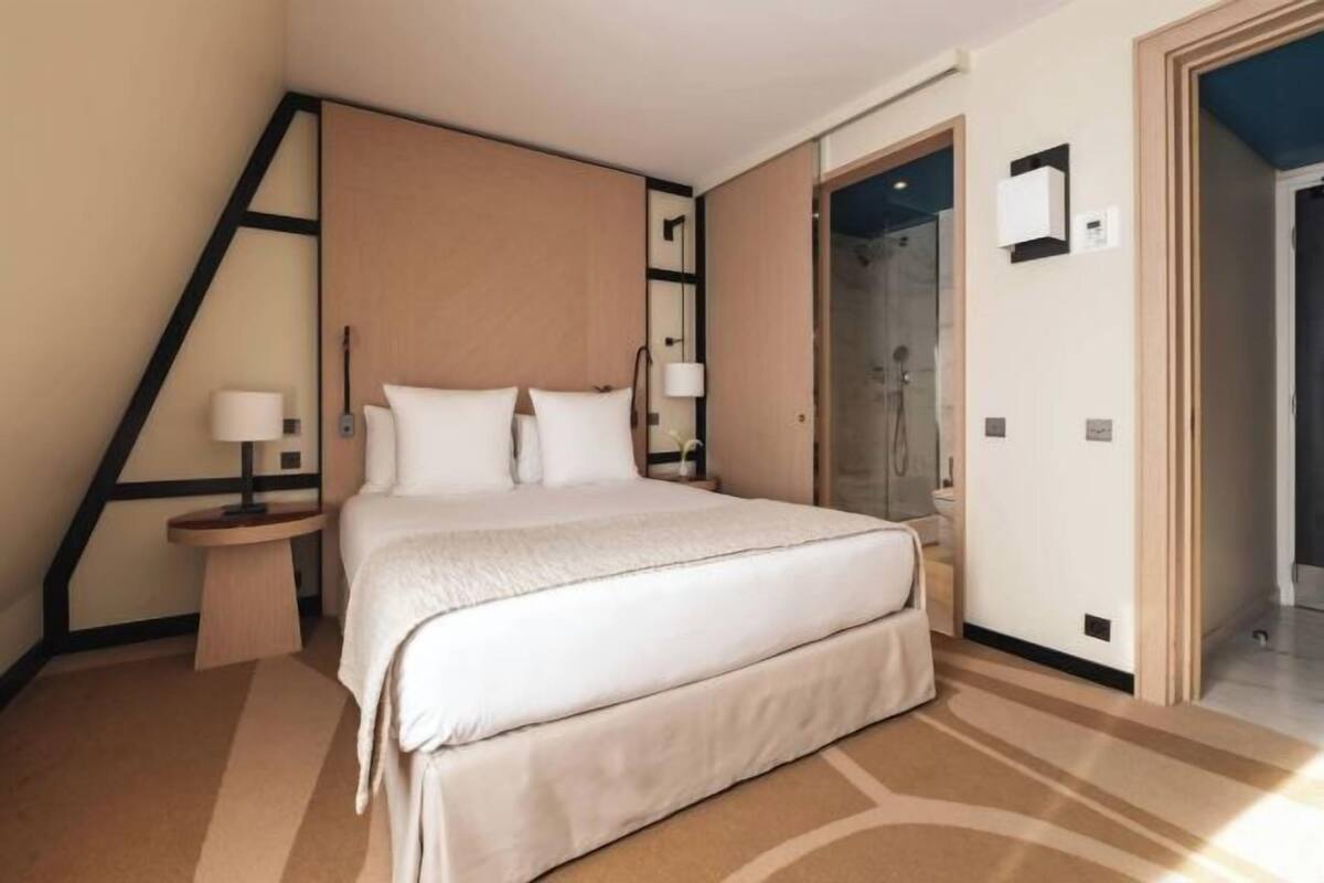 A hotel room with a large bed, bedside tables, a shower area, and a door leading to another room.