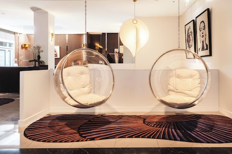 A modern interior with two hanging chairs, a patterned rug, and artwork on the walls.