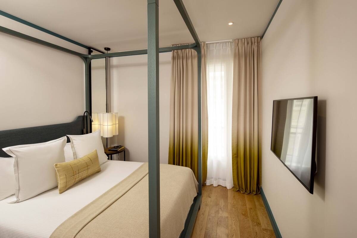 A hotel room with a bed, curtains, a TV, and a nightstand.