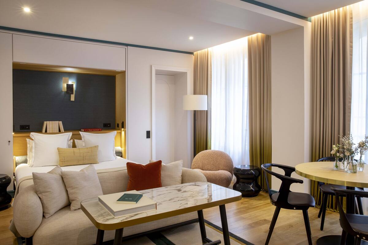A modern hotel room with a bed, a sofa, a dining table, and a chair.
