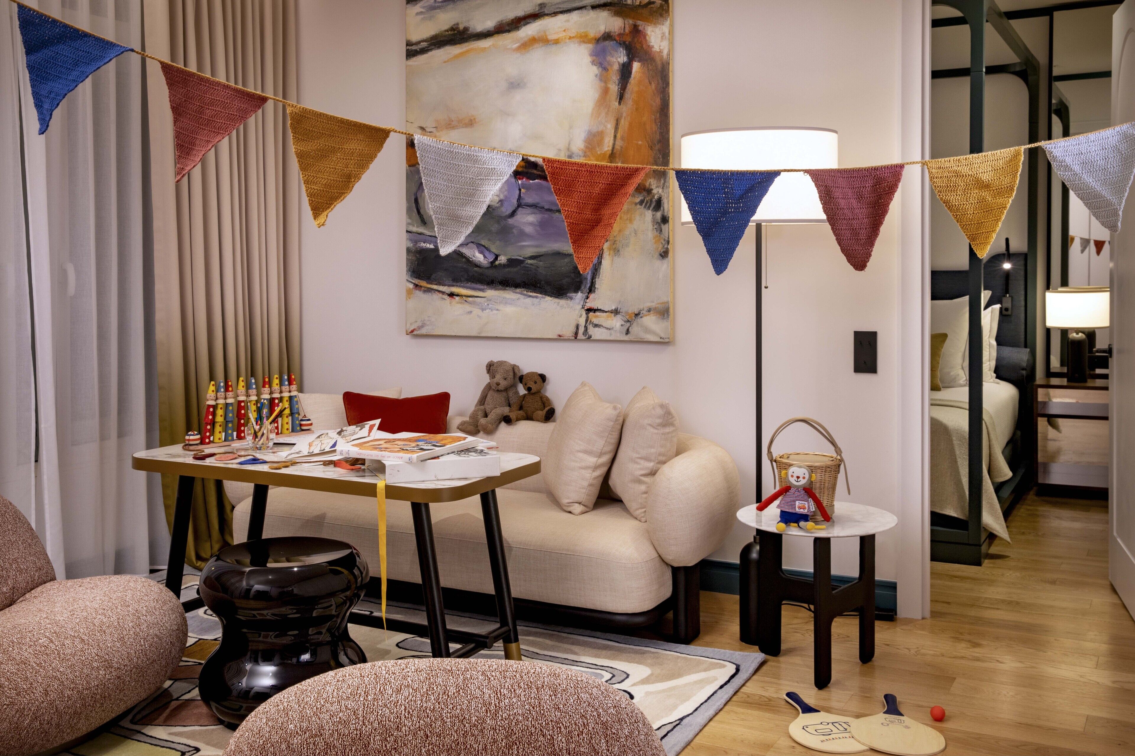 A cozy living room with a sofa, a coffee table, and a lamp. There is a painting on the wall and a window with curtains.