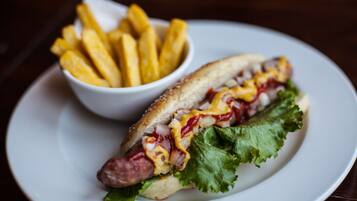 Een hotdog met sla en saus in een broodje, samen met een klein schaaltje friet op een wit bord.