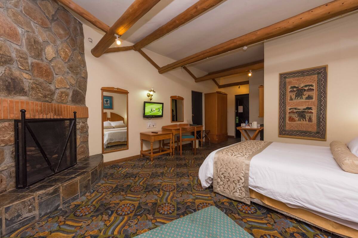 Um quarto com lareira de pedra, cama, escrivaninha e televisão.