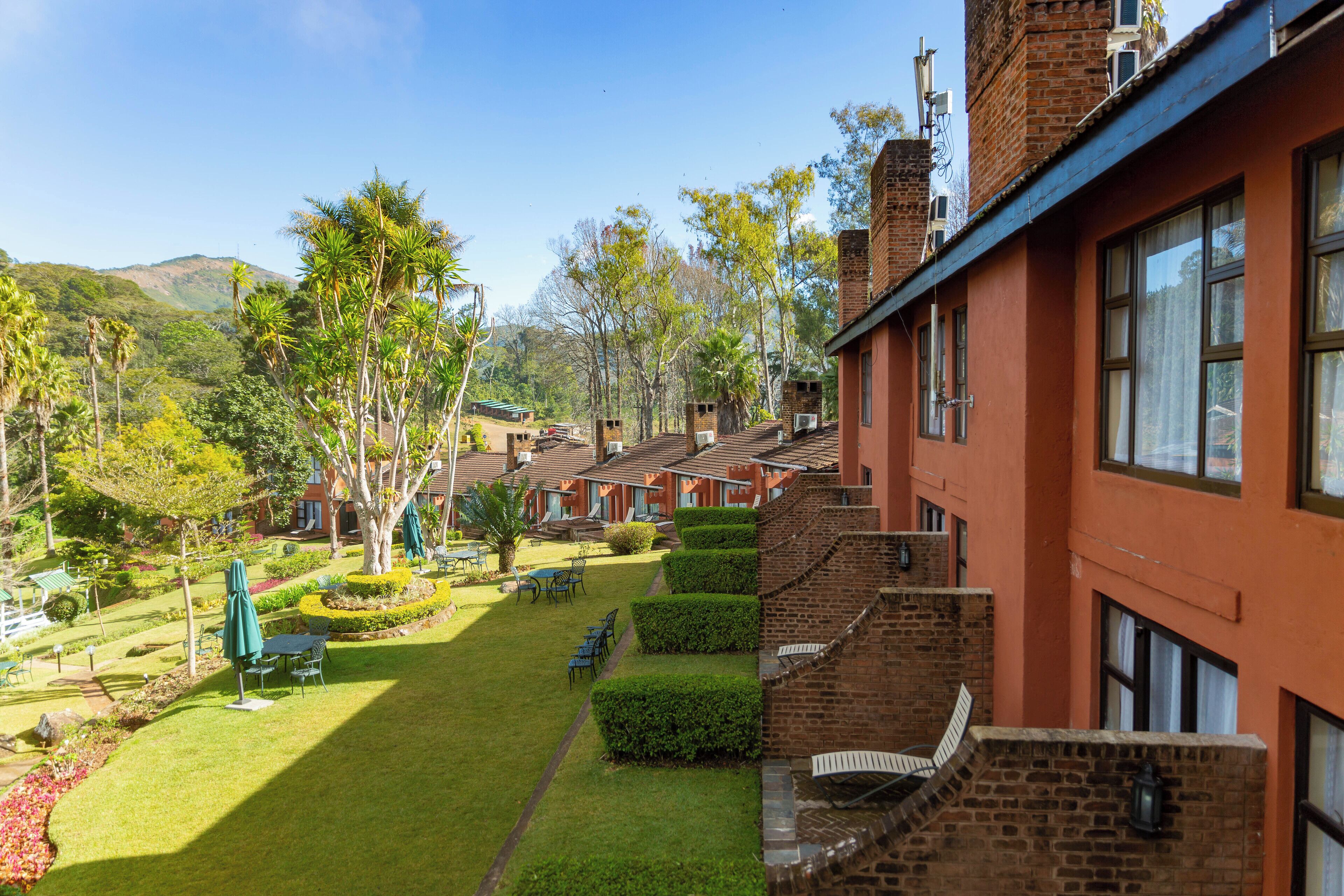 A courtyard with neatly trimmed hedges, outdoor seating, and a view of a mountain range.