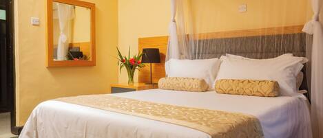 A neatly made bed with a canopy, a bedside table with a lamp, and a mirror on the wall.