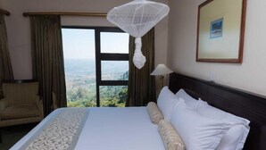 A hotel room with a large bed, a chair, a window with a view, and a hanging light fixture.