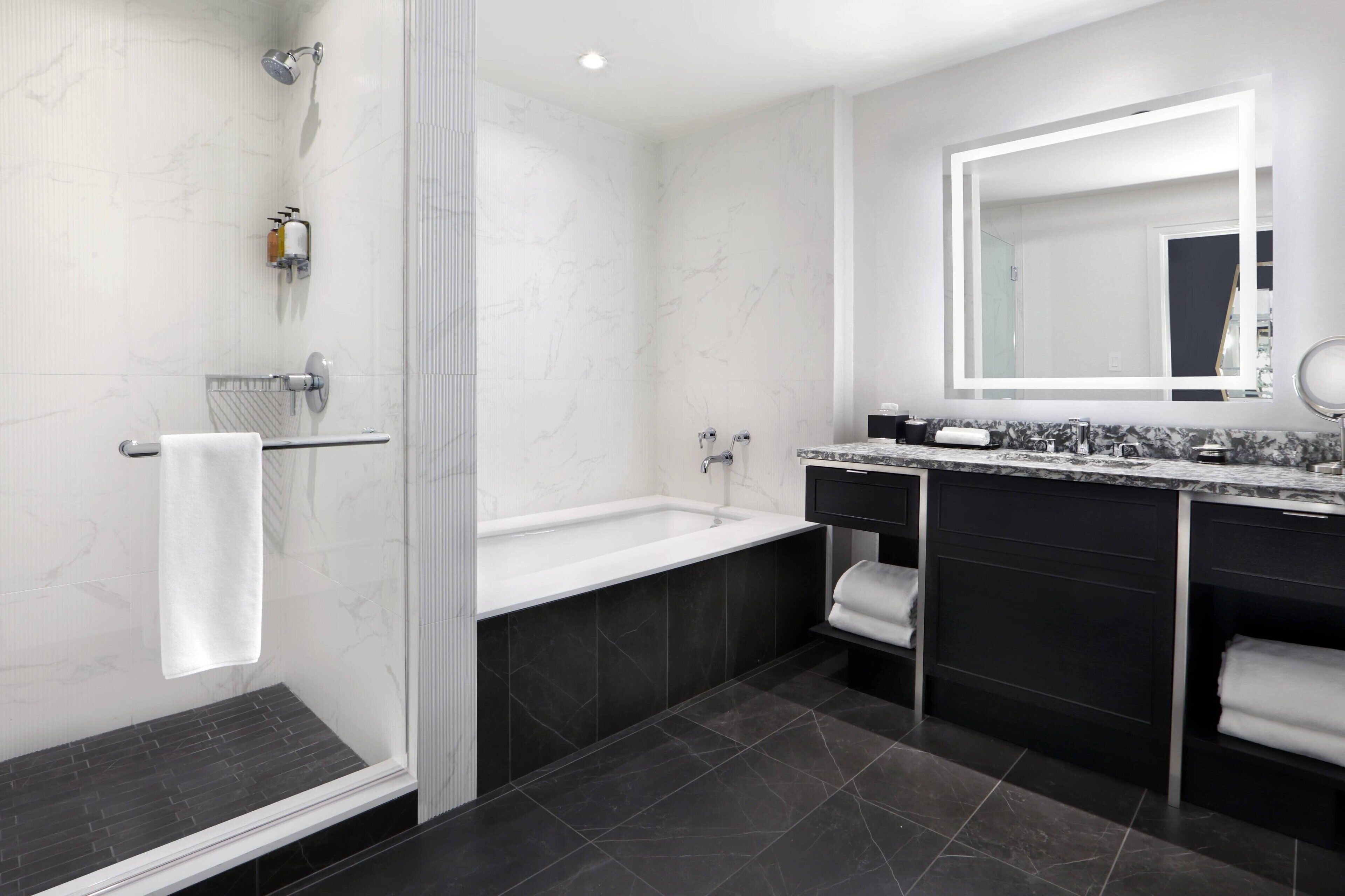 Ein modernes Badezimmer mit bodengleicher Dusche, einer Badewanne, einem großen Spiegel und einem Waschtisch mit Marmorplatte.