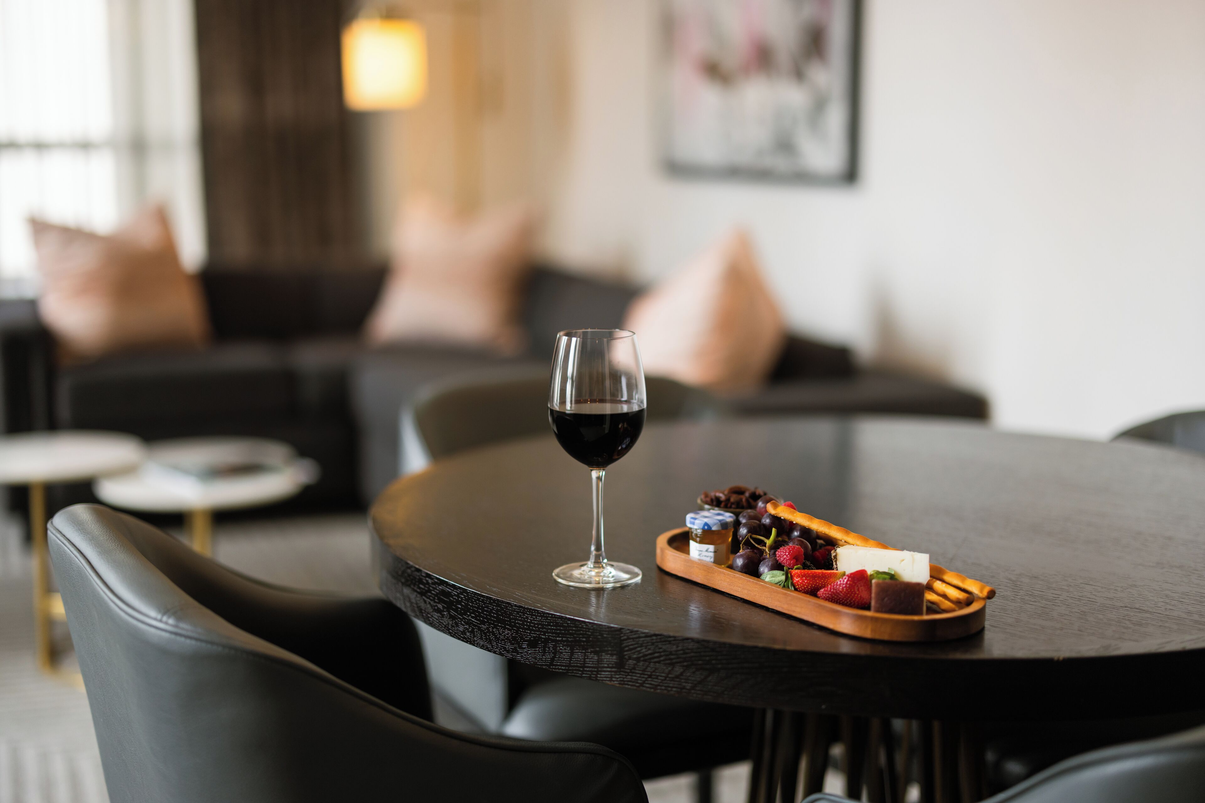 Una mesa de comedor con una copa de vino tinto, una bandeja de fruta y una mesa de madera oscura.