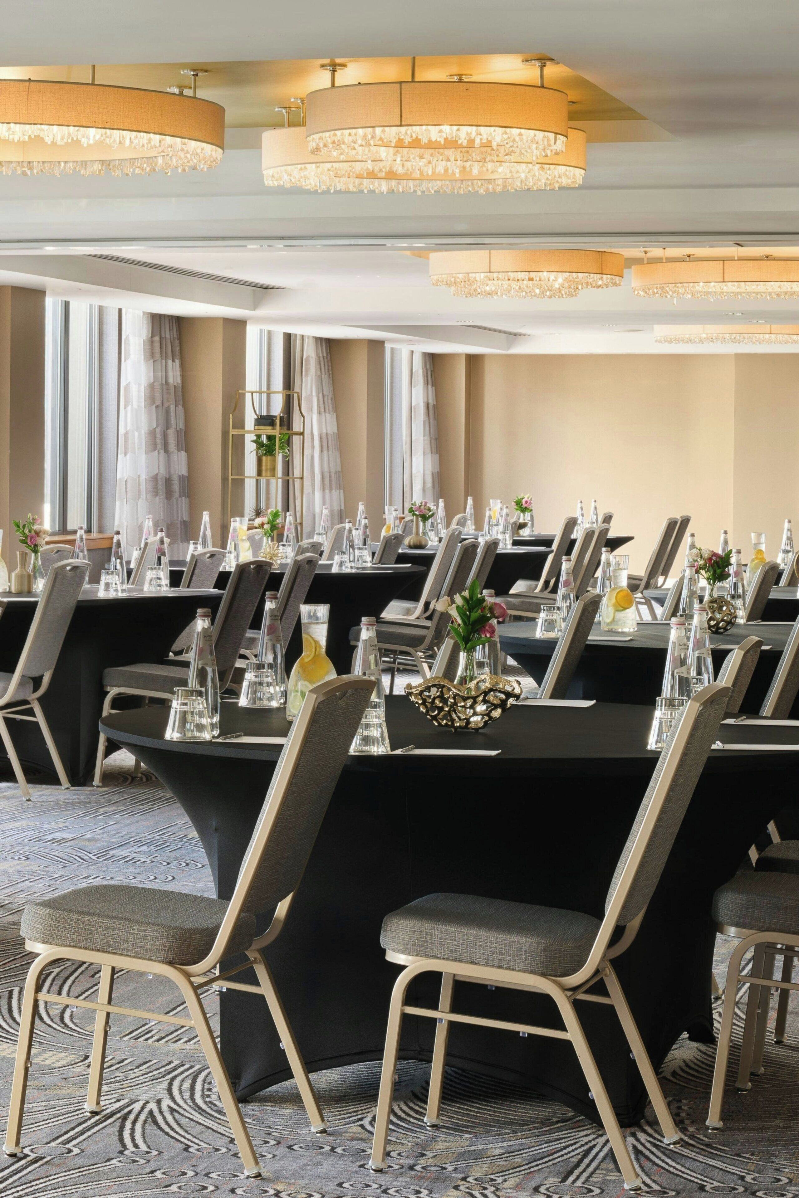 A conference room with round tables, chairs, and chandeliers.