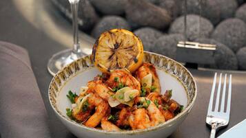 A bowl of food with a glass of white wine and a fork on a table with a fire in the background.