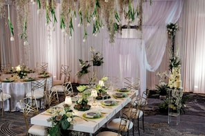 A banquet hall with long tables set for a formal event, featuring elegant table settings, chairs, and floral decorations.