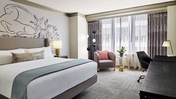 Habitación de hotel con una cama grande, un escritorio, una silla, una mesita con una planta y un mural decorativo en la pared.