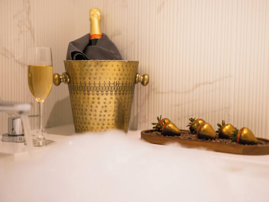 A champagne bottle in a decorative gold bucket, a glass of champagne, and a tray with golden strawberries.