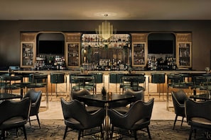 A bar area with multiple tables and chairs, a large chandelier, and shelves of bottles.